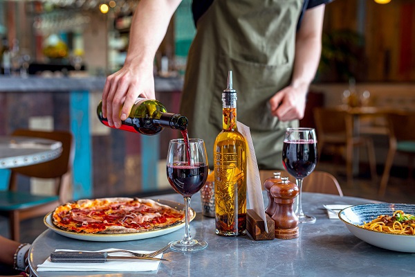 Restaurant waitress pouring a glass of red wine for customer at their table