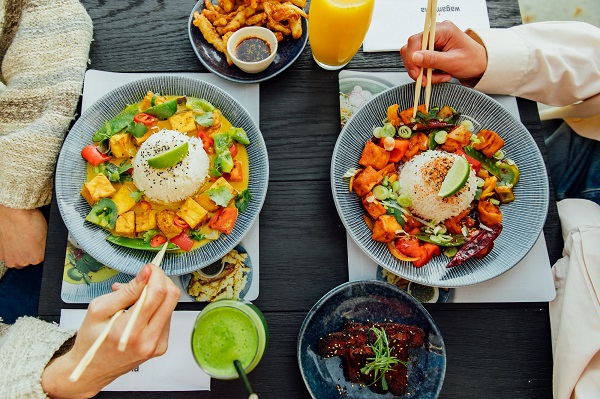 A photo of a table with wagamama food in bowls and the hands of two people eating with chopsticks